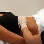 Therapist performing gentle abdominal massage on a client during a colonic hydrotherapy treatment at Redmayne Lodge, York